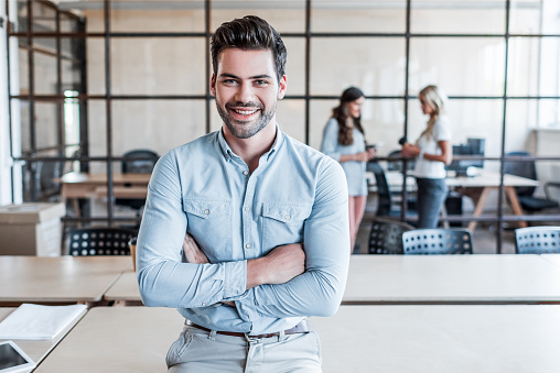 handsome young businessman with crossed arms smiling at camera in office