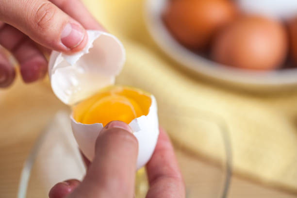 istock Woman hands breaking an egg to separate egg white and yolks, egg shells at the background 1059180978