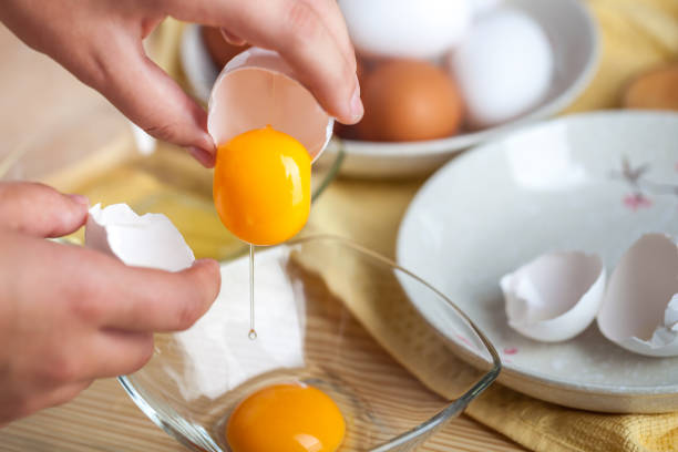 istock Woman hands breaking an egg to separate egg white and yolks, egg shells at the background 1059181022