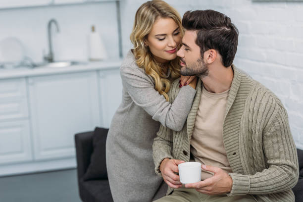 istock girlfriend hugging boyfriend and he holding cup of tea in kitchen 1059202504