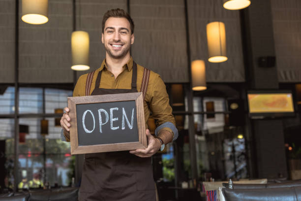 istock attractive smiling waiter holding chalkboard with open inscription in cafe 1059204918