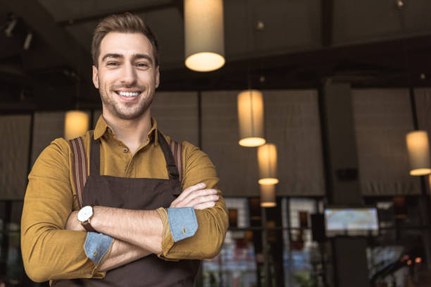 istock smiling young waiter with crossed arms looking at camera in cafe 1059204956