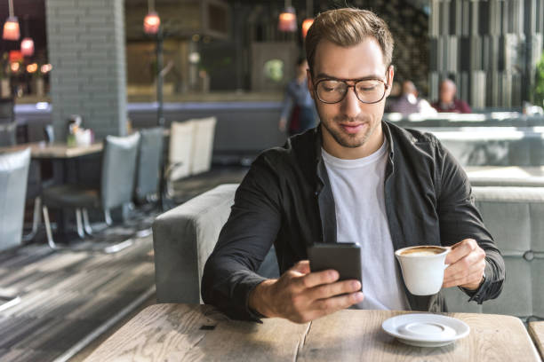 istock attractive young man with cup of coffee using smartphone in cafe 1059205216