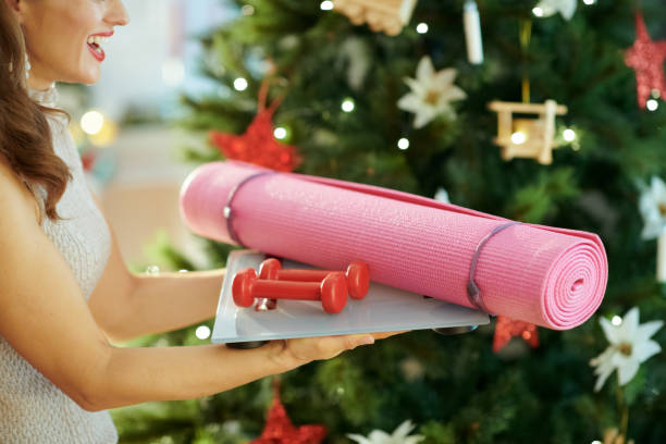 sonriente mujer joven cerca de árbol de navidad con equipo de fitness - holiday healthy lifestyle weight christmas fotografías e imágenes de stock