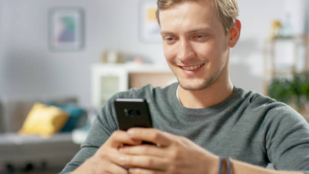 istock Portrait of the Handsome Young Man Using Smartphone, Browsing in Internet, Checking Social Networks while Sitting At Home. 1059208082