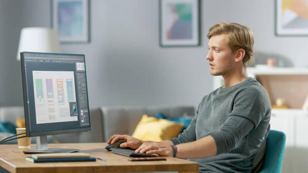 istock Handsome Focused Young Man Works on a UX / UI Mobile App Template, Uses Personal Computer while Sitting at His Desk in the Cozy Apartment. 1059208180