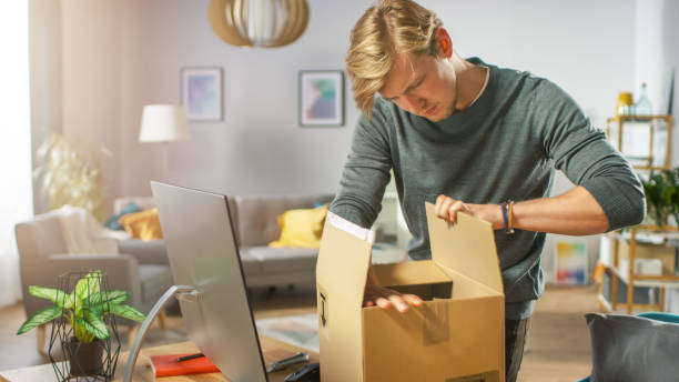 istock Handsome Young Man in Living Room with Cardboard Box Package, Opening it With Interest. 1059208320