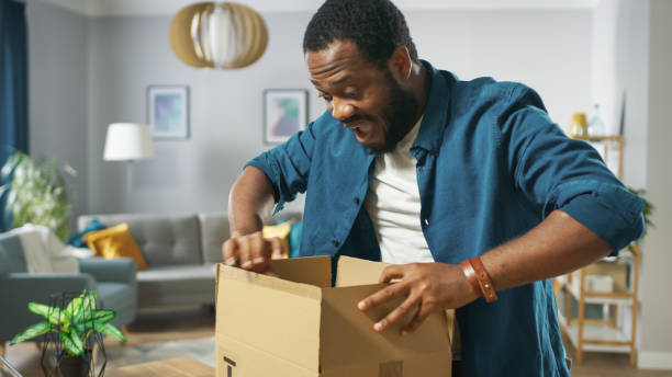 istock Handsome Excited Man Opens Cardboard Box Postal Package and Is Very Excited and Happy with Content. Man Package Unboxing. 1059208358