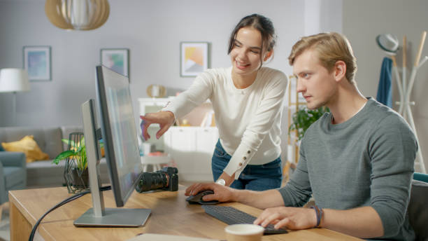 istock Male and Female Professional Editors Talk while Working in Photo Editing App / Software on a Personal Computer. Photo Editors Retouching Photos of a Beautiful Girl. Mock-up Software Design. Female Points at the Screen. 1059208474