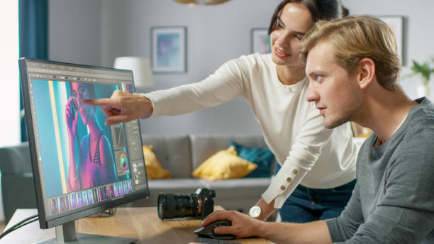istock Male and Female Professional Editors Talk while Working in Photo Editing App / Software on a Personal Computer. Photo Editors Retouching Photos of a Beautiful Girl. Mock-up Software Design. Female Points at the Screen. 1059208492