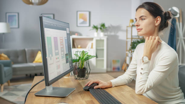 istock Beautiful Female Software Designer Works on a UX / UI Mobile App Template, Uses Personal Computer. Freelance Programmer Working from Home. Mock-up App Design. 1059208534
