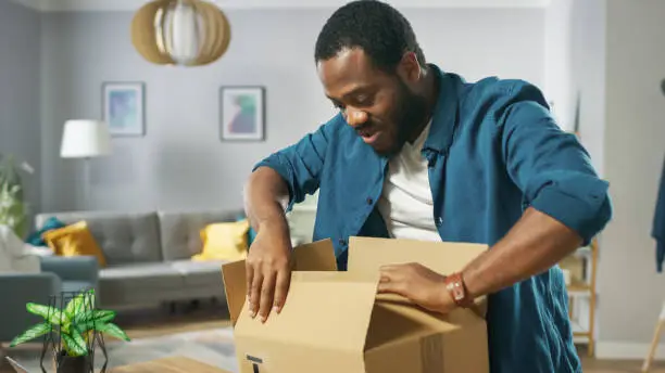 Photo of Handsome Excited Man Opens Cardboard Box Postal Package and Is Very Happy with Content. Man Package Unboxing.