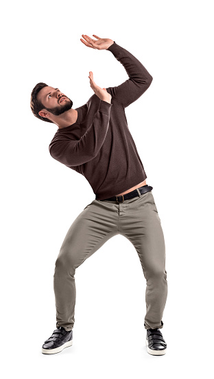 A bearded man in casual garb stands protecting himself with outstretched hands from something getting to him from above. Dangerous position. Big problems. Weight of repercussions.
