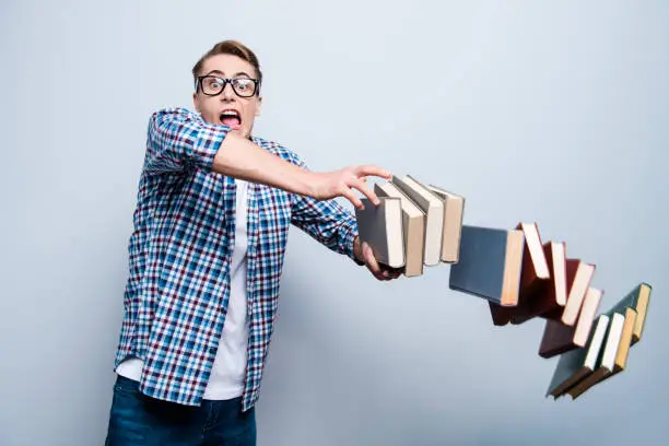 Photo of Portrait of fail man in street style wear, stumbled and scattered books on the floor isolated on light blue gray background