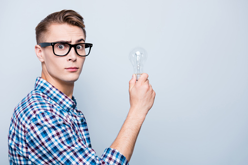 Profile side view photo of good-looking high school guy in checkered shirt and white t-shirt look at camera, hold lamp in hands isolated on light gray background with copy space for text