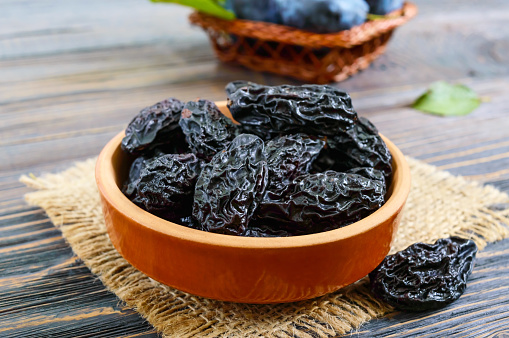 Prunes in a clay bowl and fresh plums, leaves on a wooden table. Fresh prunes for healthy life.