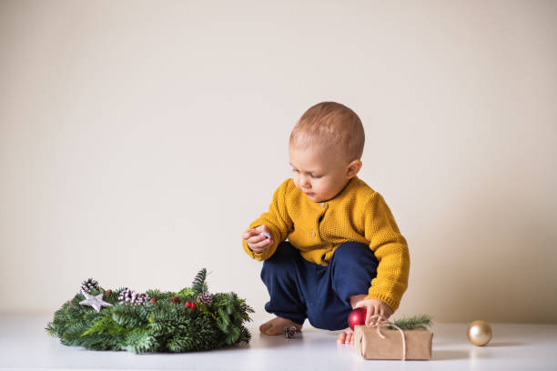 un niño pequeño y una corona de navidad en una mesa. - mano sobre cadera fotografías e imágenes de stock
