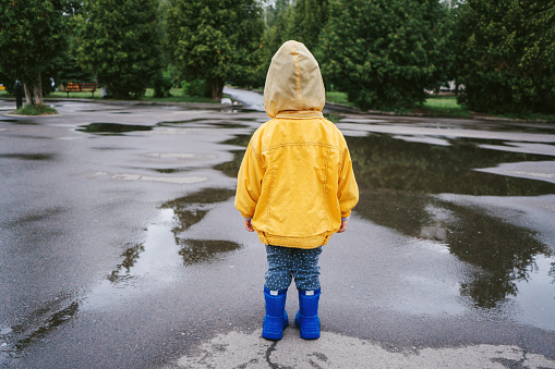 Little boy in yellow raincoat  walking outdoors and jumping on puddle