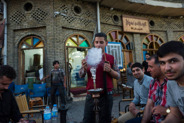 Smoking shisha at Machko cafe in Erbil, Iraq Erbil, Iraq - May 4, 2017: A young man sets up a waterpipe, or shisha, for customers to smoke at Machko, a famous cafe at the base of the citadel in Erbil, Iraq. iraqi kurdistan stock pictures, royalty-free photos & images
