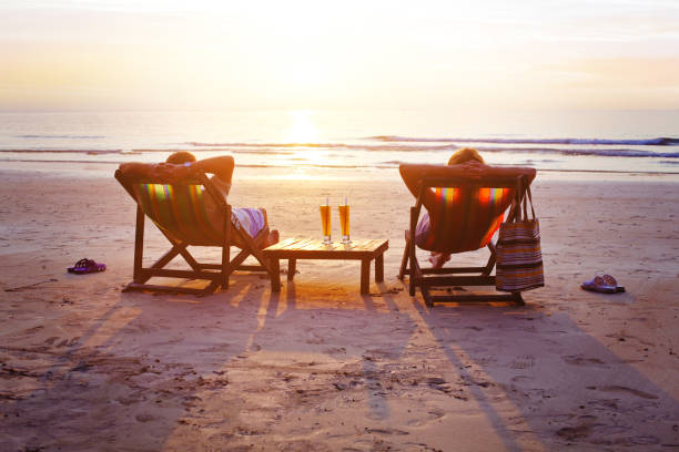 Vacation travel, silhouettes of happy couple relaxing on beach. honeymoon travel, silhouettes of happy couple relaxing in deck chairs on the beach at sunset beach holiday stock pictures, royalty-free photos & images