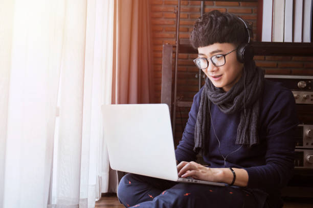 Cтоковое фото Молодой азиатский студент в свитере учится на компьютерном ноутбуке и слушает музыку в гостиной