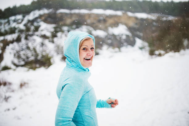 Senior woman runner resting in winter nature, a hood on her head.