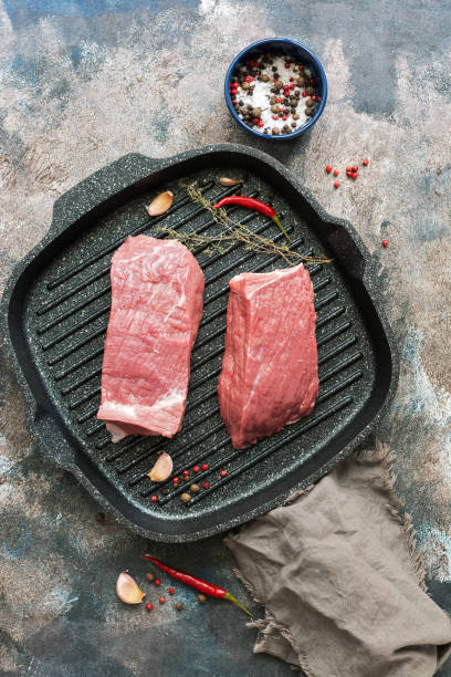 istock Raw beef tenderloin with spices in a frying pan for cooking. Rustic background, top view, flat lay. 1059288140