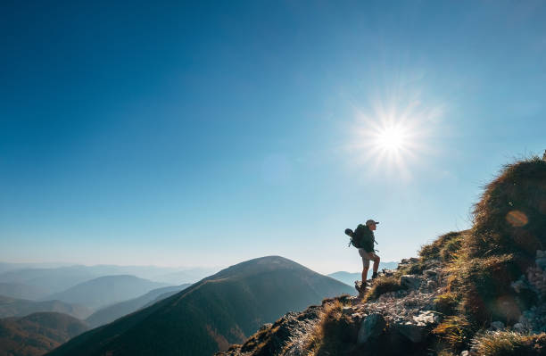 istock Boy backpacker traveler walk up on mountain top in contrast sun light 1059309260