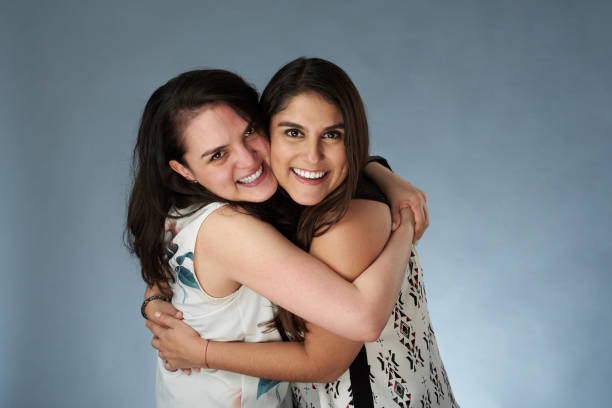 Two young smiling girl friends hugging on studio background