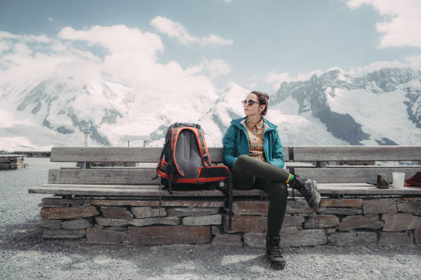 Woman sitting on bench on the background of  the glacier in Swiss alps Young Caucasian woman with backpack sitting on bench  near the glacier in Swiss alps sitting on bench stock pictures, royalty-free photos & images