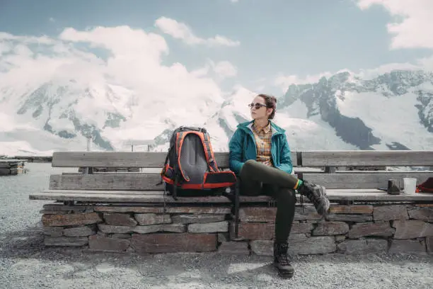 Young Caucasian woman with backpack sitting on bench  near the glacier in Swiss alps