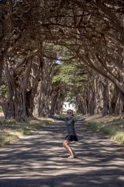 Caucasian female raises arms up at the Cypress Tree Tunnel on Point Reyes National Seashore in Marin County in Northern California