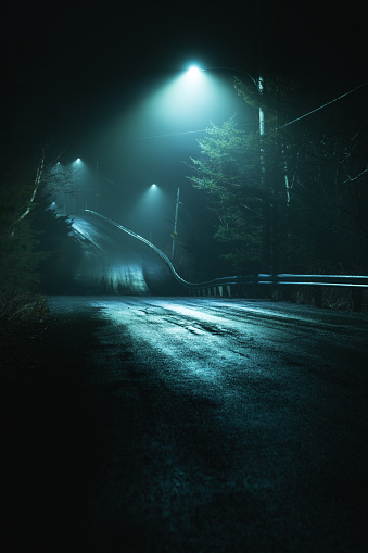 A dirt road is illuminated by a series of street lights on a moody foggy night.