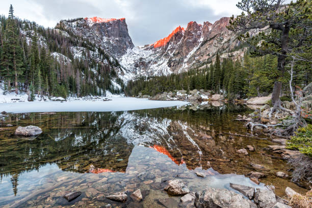 Amber Peaks above Dream Lake Hallette Peak and Flattop Mountain glow pink at sunrise, reflected in Dream Lake in Rocky Mountain National Park. hallett peak stock pictures, royalty-free photos & images