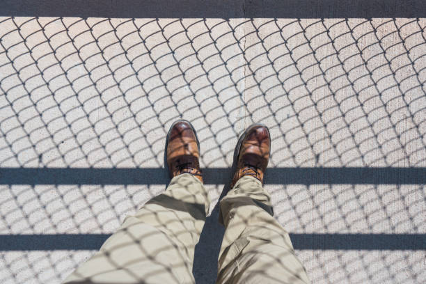 istock Man standing on road with fence shadow 1059347692