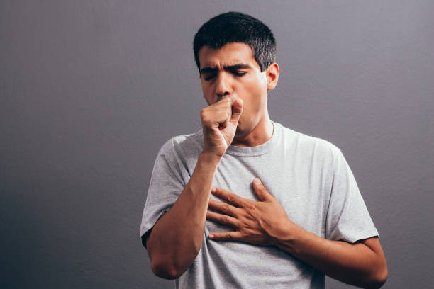 man coughing into his fist, isolated on a gray background - going into imagens e fotografias de stock