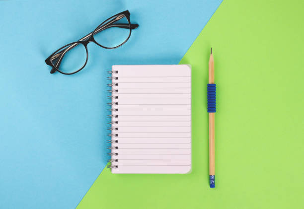 istock Spiral notepad, pencil and glasses on pastel background. 1059377422