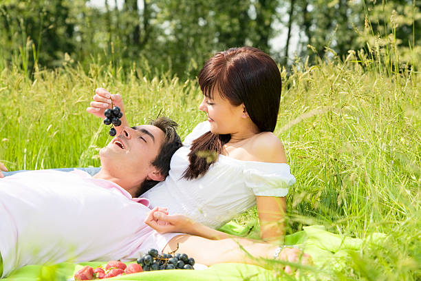 meadow Couple lying in grass, smiling and eating grapes feeding grapes stock pictures, royalty-free photos & images