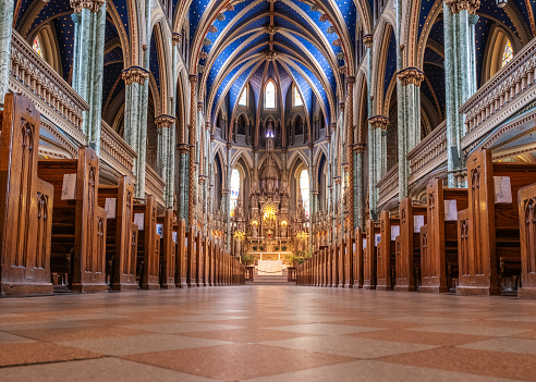 Ottawa, Ontario, Canada - September 4, 2018: Inside the Notre-Dame Cathedral Basilica, a unique low perspective looking along the rows of pews up to the beautifully ornate alter and cathedral recess with a blue domed roof.