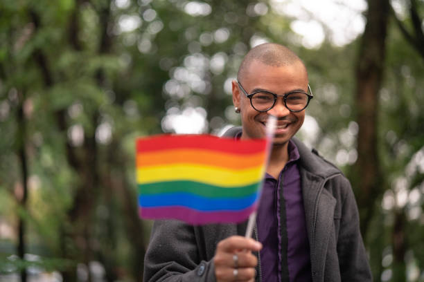 hombre gay ondeando la bandera del arco iris - gay pride rainbow flag homosexual fotografías e imágenes de stock