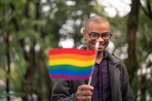 homme gay africain brandissant le drapeau arc-en-ciel - gay pride flag gay pride gay man homosexual photos et images de collection