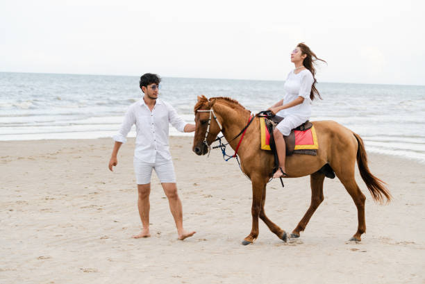 istock Young couple goes horse riding on tropical beach. 1059426432