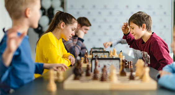 Kids of different ages, boys and girls, playing chess on the tournament in the chess club