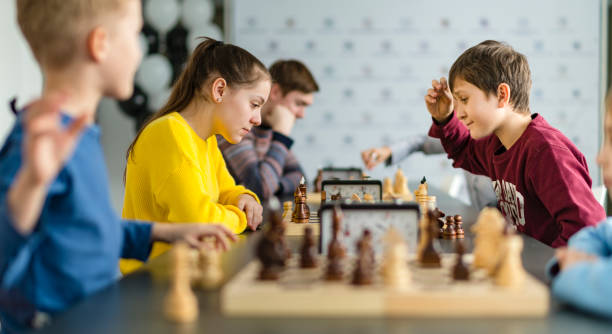 Kids of different ages, boys and girls, playing chess on the tournament in the chess club stock photo