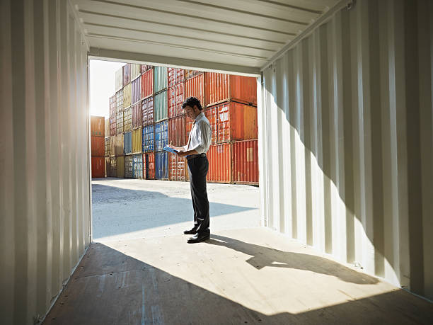 business man with shipping containers portrait of mid adult businessman standing near cargo container and writing on clipboard. Horizontal shape, side view, copy space warehouse containers stock pictures, royalty-free photos & images