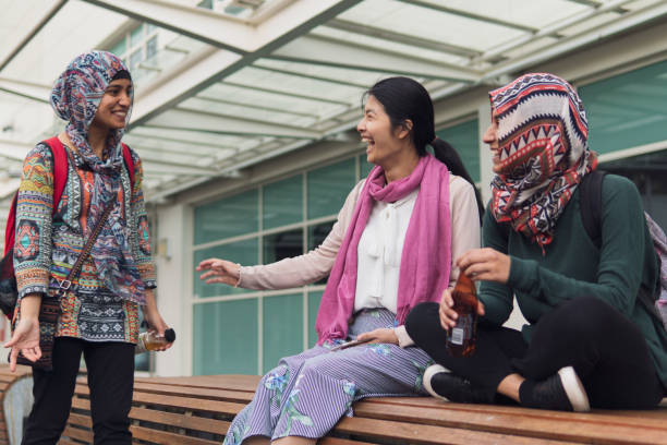 Muslim University student greeting her friends sitting outside on a bench stock photo