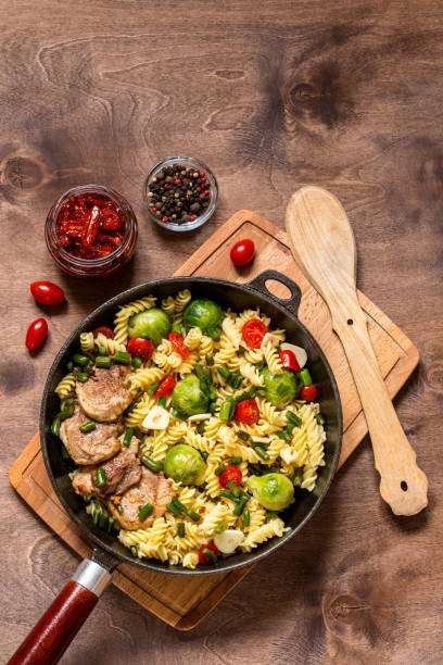 istock Pasta with vegetables in cast iron pan on wooden background 1059452922