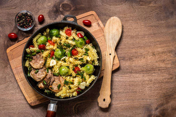 istock Pasta with vegetables in cast iron pan on wooden background 1059452934