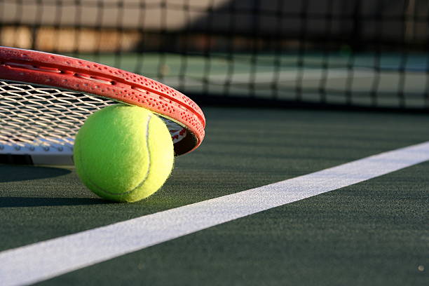 Tennis Ball & Racket on a Green Outdoor Court Tennis racket lying on a tennis ball near the net and court line sports court photos stock pictures, royalty-free photos & images