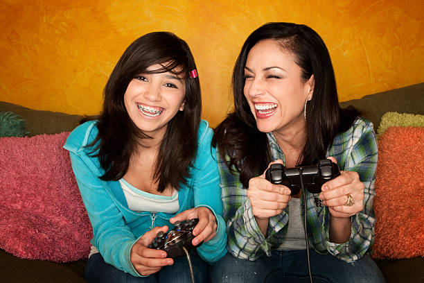 Hispanic Woman and Girl Playing Video game Attractive Hispanic Woman and Girl Playing a Video Game with Handheld Controllers girl flex stock pictures, royalty-free photos & images